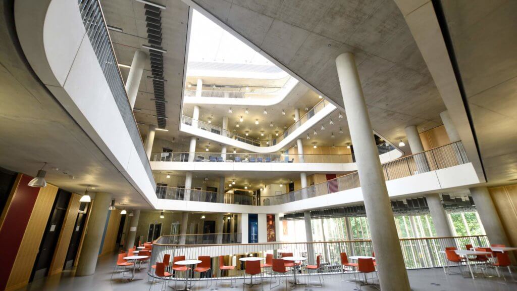 Image of an open concept university building with modern seating arrangements and large windows allowing ample natural light to fill the space